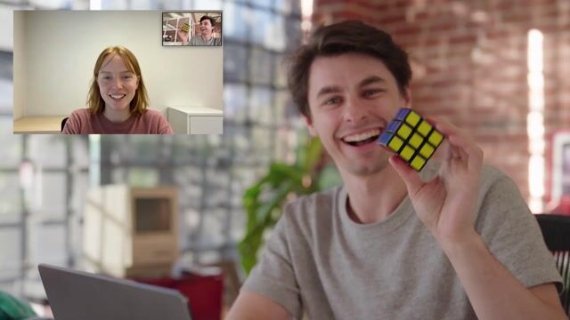 A split-screen video call: a man holds up a largely solved Rubik's cube on one side while the generated Tavus persona watches on the other.